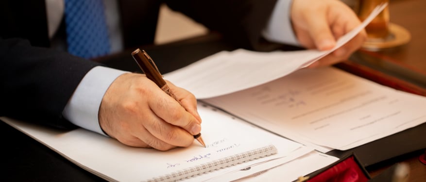 Un notaire en costume signe un document officiel sur un bureau en bois